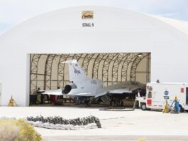 X-59 Powers Up Engine for Initial Takeoff View from outside a large run stall. The 100-foot-long X-59 sits in the run stall with the engine and the rest of the back of the aircraft sitting outside the run stall’s open bay door.