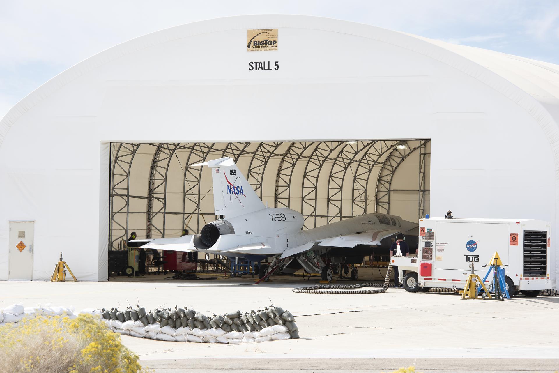 afrc2024 0176 01large.jpg View from outside a large run stall. The 100-foot-long X-59 sits in the run stall with the engine and the rest of the back of the aircraft sitting outside the run stall’s open bay door.
