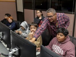 NASA Experts Inspire Students with Perseverance Stories A group of people are sitting at a desk looking at computers with headsets on. A man is pointing and smiling at one of the computer screens.