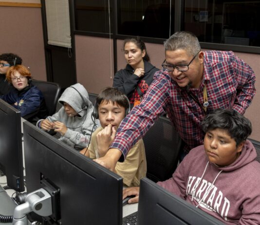NASA Experts Inspire Students with Perseverance Stories A group of people are sitting at a desk looking at computers with headsets on. A man is pointing and smiling at one of the computer screens.