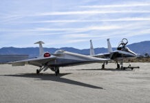 NASA’s X-59 Successfully Finishes Electromagnetic Testing A NASA F-15 aircraft sits 20 feet off the left side of the X-59 aircraft, with a white hangar and hills in the background, during electromagnetic interference testing.