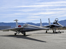 NASA’s X-59 Successfully Finishes Electromagnetic Testing A NASA F-15 aircraft sits 20 feet off the left side of the X-59 aircraft, with a white hangar and hills in the background, during electromagnetic interference testing.