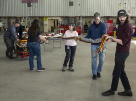 NASA Analyzes Lunar Light to Enhance Earth Monitoring A team of people carry a science instrument across a hangar floor. Two men at the back left of the frame roll a cart carrying the instrument body while four others ahead of the cart walk toward the right of the frame carrying a heavy twine of cables attached to the instrument.
