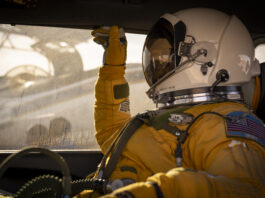 NASA ER-2 Pilot Readies for GEMx Mission Flight A person facing left sits inside a vehicle. They are wearing a yellow jumpsuit and gloves and a white helmet with a visor that looks like a smaller version of the kind astronauts wear during spacewalks. Outside of the window behind the person, you can see the ER-2 aircraft being prepared for flight.
