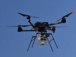 NASA Experiments with Supersonic Parachute Delivery System A drone with four rotors hoovers against a canvas of deep blue sky prior to releasing the experiment it carries high above the desert floor.