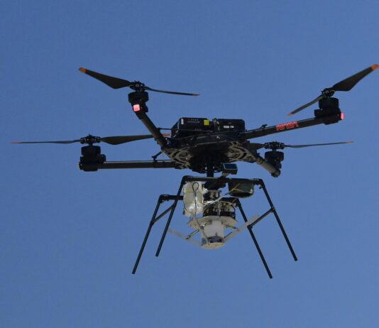 NASA Experiments with Supersonic Parachute Delivery System A drone with four rotors hoovers against a canvas of deep blue sky prior to releasing the experiment it carries high above the desert floor.