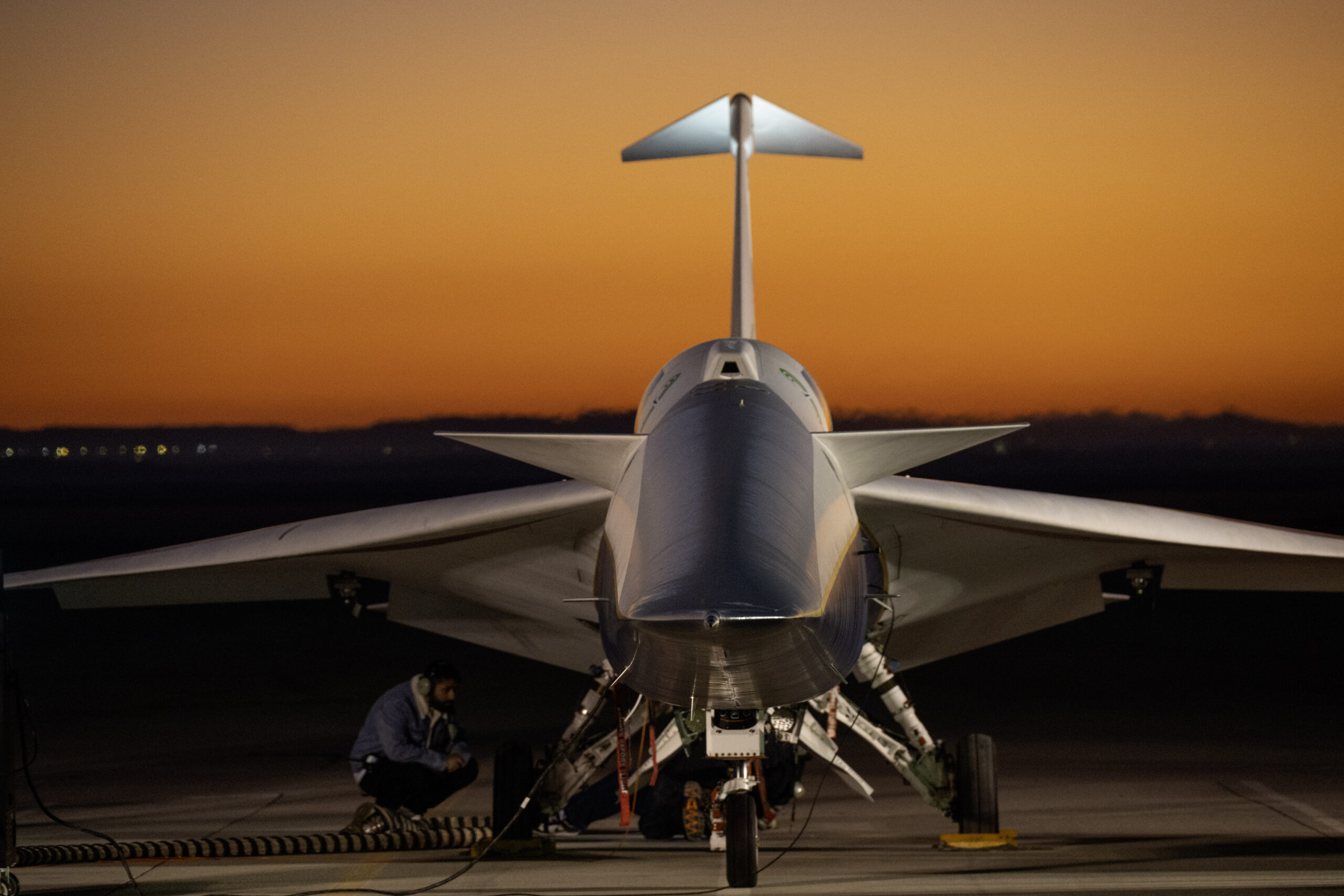 An aircraft resting on a section of runway as seen from the front, with its nose facing the camera. The early morning sky is orange in the background.