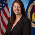 Aubrie Henspeter Heads NASA’s Commercial Moon Ventures A woman dressed in a black suit stands in front of a blue background.