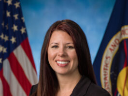 Aubrie Henspeter Heads NASA’s Commercial Moon Ventures A woman dressed in a black suit stands in front of a blue background.
