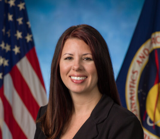 Aubrie Henspeter Heads NASA’s Commercial Moon Ventures A woman dressed in a black suit stands in front of a blue background.