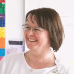 Revolutionizing Hospital Scheduling with AI: A New Era in Healthcare Smiling woman with glasses near colorful wall pegs.