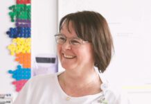 Revolutionizing Hospital Scheduling with AI: A New Era in Healthcare Smiling woman with glasses near colorful wall pegs.