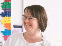 Revolutionizing Hospital Scheduling with AI: A New Era in Healthcare Smiling woman with glasses near colorful wall pegs.