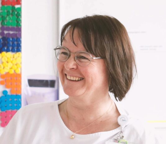 Revolutionizing Hospital Scheduling with AI: A New Era in Healthcare Smiling woman with glasses near colorful wall pegs.