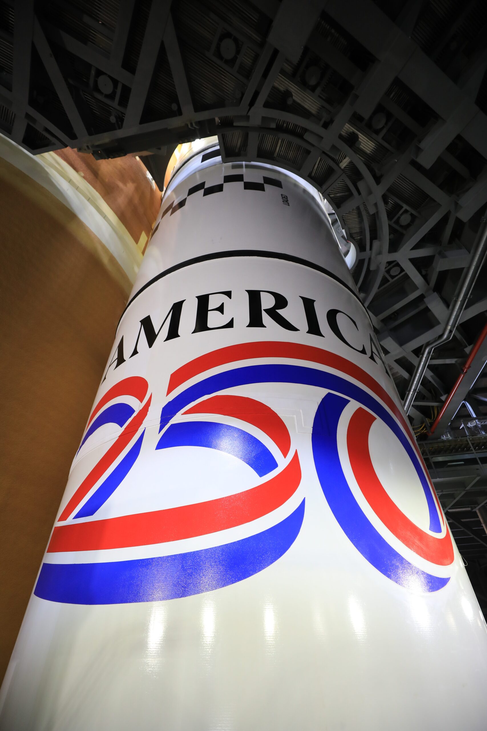 Image shows the America 250 logo in black, red, blue colors painted on the white solid rocket boosters of NASA