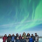 NASA Encourages Aspiring Scientists with Eclipses and Auroras A group of 13 people standing together on snow-covered ground, dressed in warm winter clothing, with the aurora glowing in the sky above them. Some are kneeling, while others stand in front of them, all facing the camera and smiling.
