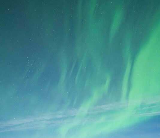 NASA Encourages Aspiring Scientists with Eclipses and Auroras A group of 13 people standing together on snow-covered ground, dressed in warm winter clothing, with the aurora glowing in the sky above them. Some are kneeling, while others stand in front of them, all facing the camera and smiling.