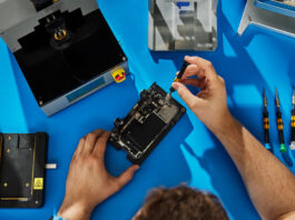 Apple expands repair options by supporting genuine used parts Technician repairing smartphone on blue workbench.