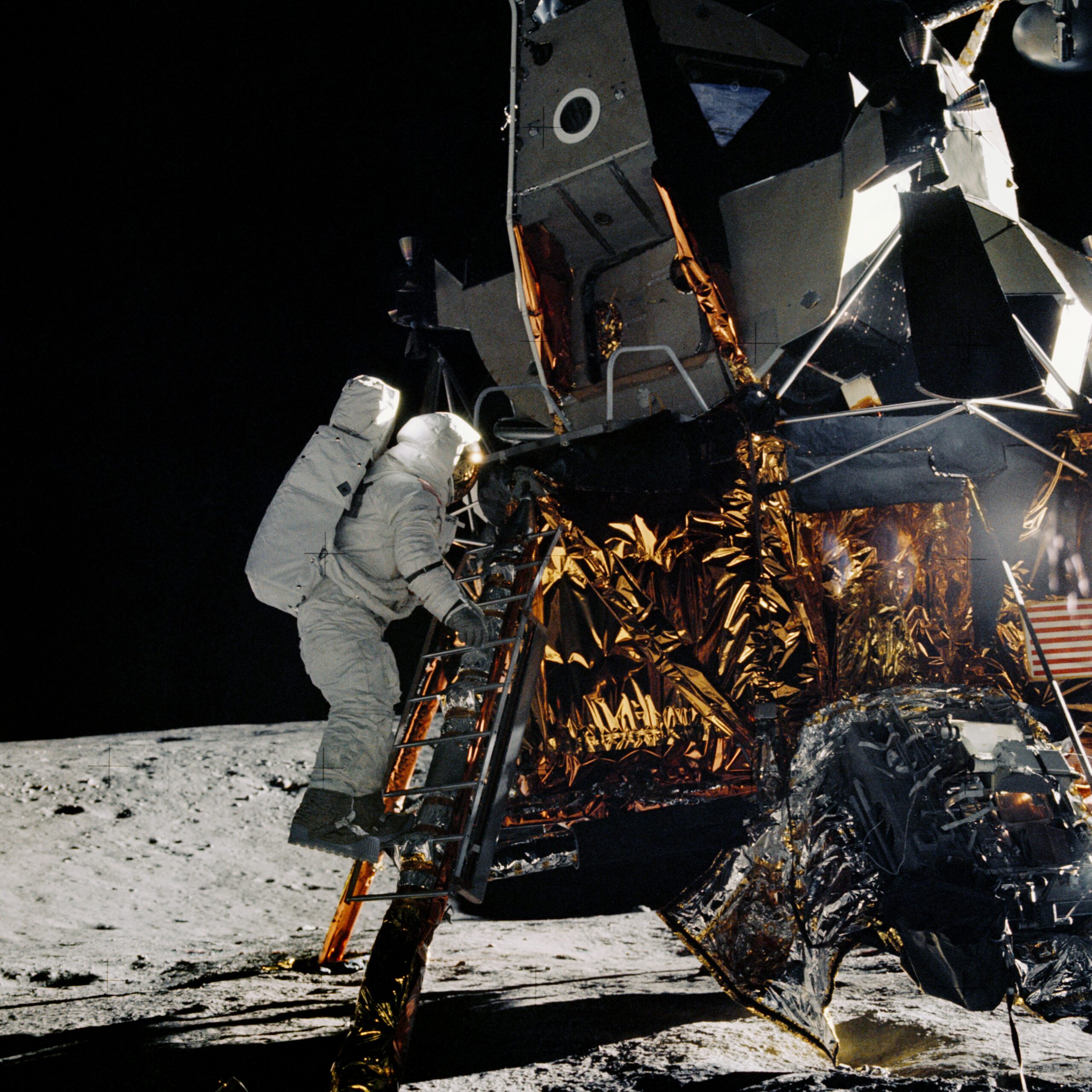 as12 46 6728orig.jpg On the Moon, an astronaut in a white spacesuit climbs down a ladder on a lunar module. The lunar module is made of metal with gold and silver foil covering some of its lower half.