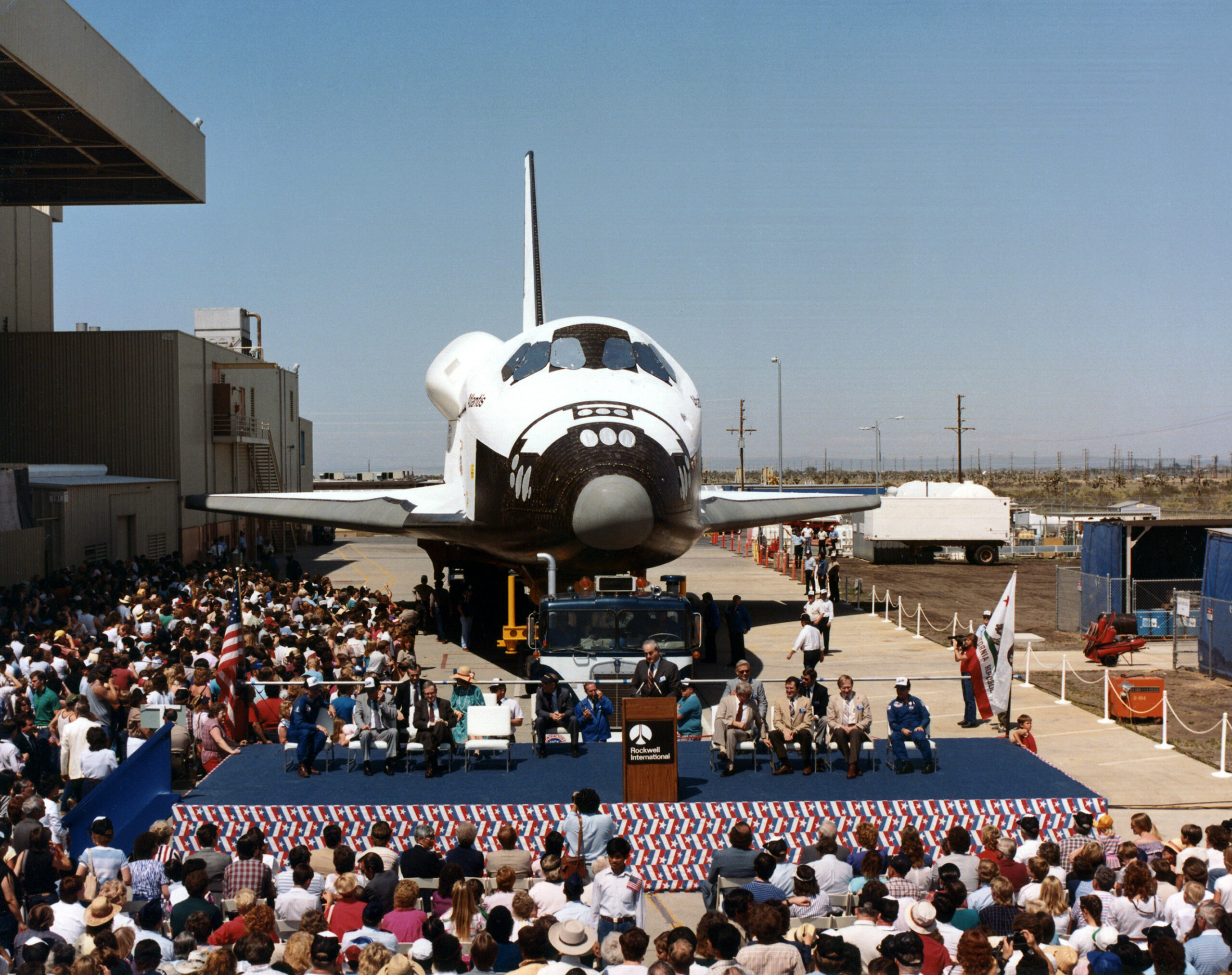 atlantis rollout 2 palmdale rollout mar 6 1985.jpg View of a space shuttle orbiter with a about a dozen people on a stage in front of it.