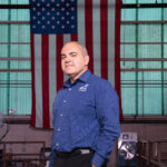 Carlos Garcia-Galan Appointed Deputy Manager of NASA’s Gateway Program Carlos Garcia-Galan poses in front of the American flag in the Electric Propulsion and Power Laboratory at NASA’s Glenn Research Center. He has a serious expression is wearing a blue long-sleeve shirt with the Artemis program logo and black pants.