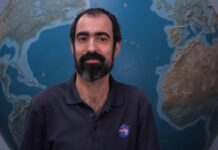 NASA’s Alfonso Delgado Bonal Explores Clouds for Research Alfonso stands in front of a large globe of Earth. He has dark hair and a beard and mustache, with a thoughtful expression. He is wearing a navy blue polo with the blue, red, and white NASA “meatball” logo on the chest patch.