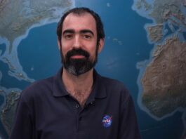 NASA’s Alfonso Delgado Bonal Explores Clouds for Research Alfonso stands in front of a large globe of Earth. He has dark hair and a beard and mustache, with a thoughtful expression. He is wearing a navy blue polo with the blue, red, and white NASA “meatball” logo on the chest patch.