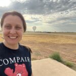 Regina Caputo Shapes the Future of High-Energy Astrophysics at NASA Regina Caputo smiles at the camera in a selfie that captures her head and shoulders. Her brown hair is tied back in a ponytail, and she is wearing a navy-blue tee-shirt which reads “COMPAIR.” Behind Regina is a large open field covered in patches of light brown and yellow grass. The sky is a hazy gray-blue and is covered in dark gray clouds that are thick in certain places but patchy. In the far distance behind Regina, nearing the horizon, is a large space-balloon. The balloon resembles a gray upside-down teardrop, the tip of which just touches the ground.