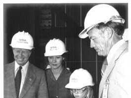 NASA Chief Honors President Carter’s Legacy President Jimmy Carter, wife Rosalynn, daughter Amy, and Kennedy Space Center director Lee Scherer, all wearing NASA hard hats, look down at a scale model of the crawler, which transported the Shuttle to the launch pad. The photo is in black and white.