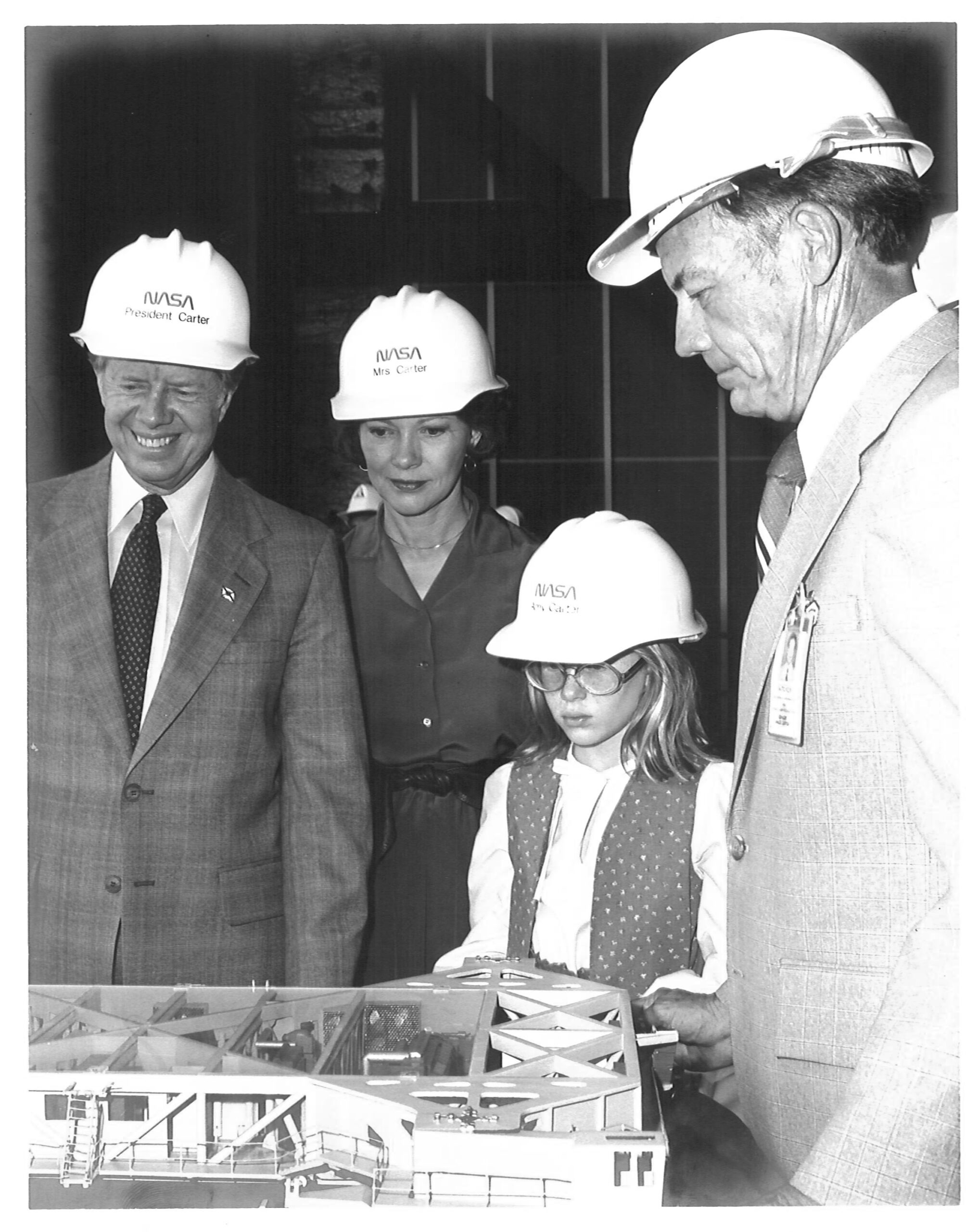 carter visit 3 2.jpg President Jimmy Carter, wife Rosalynn, daughter Amy, and Kennedy Space Center director Lee Scherer, all wearing NASA hard hats, look down at a scale model of the crawler, which transported the Shuttle to the launch pad. The photo is in black and white.