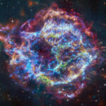 NASA’s XRISM Detects Chlorine, Potassium in Cassiopeia A This image of Cassiopeia A resembles a disk of electric light with red clouds, glowing white streaks, red and orange flames, and an area near the center of the remnant resembling a somewhat circular region of green lightning. X-rays from Chandra are blue and reveal hot gas, mostly from supernova debris from the destroyed star, and include elements like silicon and iron. X-rays are also present as thin arcs in the outer regions of the remnant. Infrared data from Webb is red, green, and blue. Webb highlights infrared emission from dust that is warmed up because it is embedded in the hot gas seen by Chandra, and from much cooler supernova debris. Hubble data shows a multitude of stars that permeate the field of view.