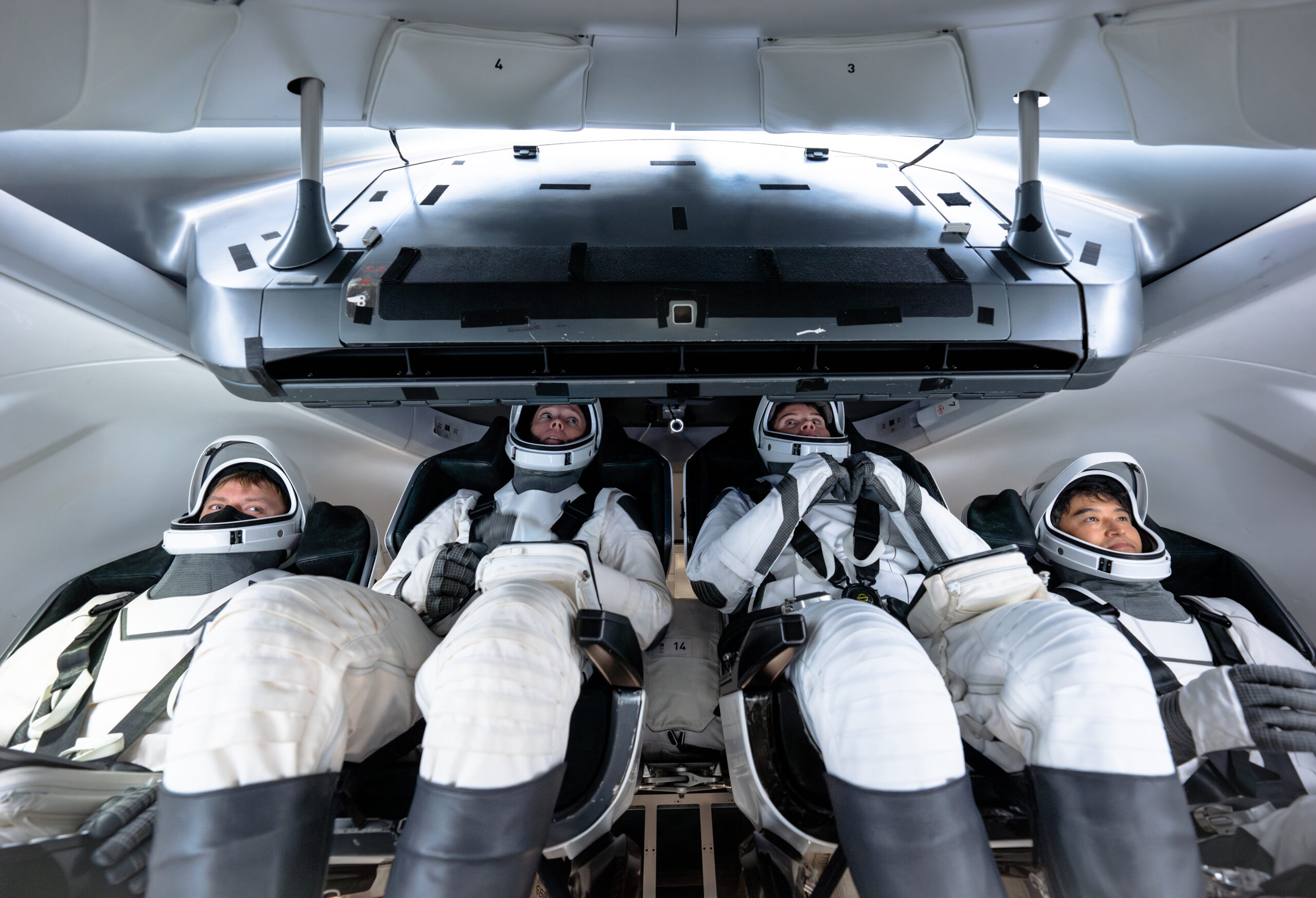crew10 atp 20240916 06403 .jpg Four NASA SpaceX Crew-10 members sit in a capsule in their white spacesuits, looking around the spacecraft during training.