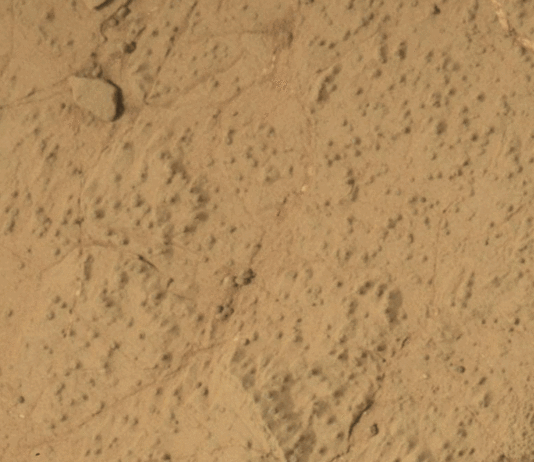 Curiosity Rover Finds Mars’ Largest Organic Molecules Yet This animated image shows a close-up view of a flat, dusty, tan-colored rock surface with fine cracks and small, dark specks scattered across it. In the animation, a hole appears in the center of the frame, with loose powdered material surrounding the hole. The surrounding rock surface remains unchanged, highlighting the freshly drilled hole and the fine texture of the rock.