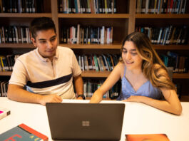 Tec de Monterrey Unveils AI-Driven Learning Environment A male and female student sit at a desk looking at a laptop, with shelves of books behind them