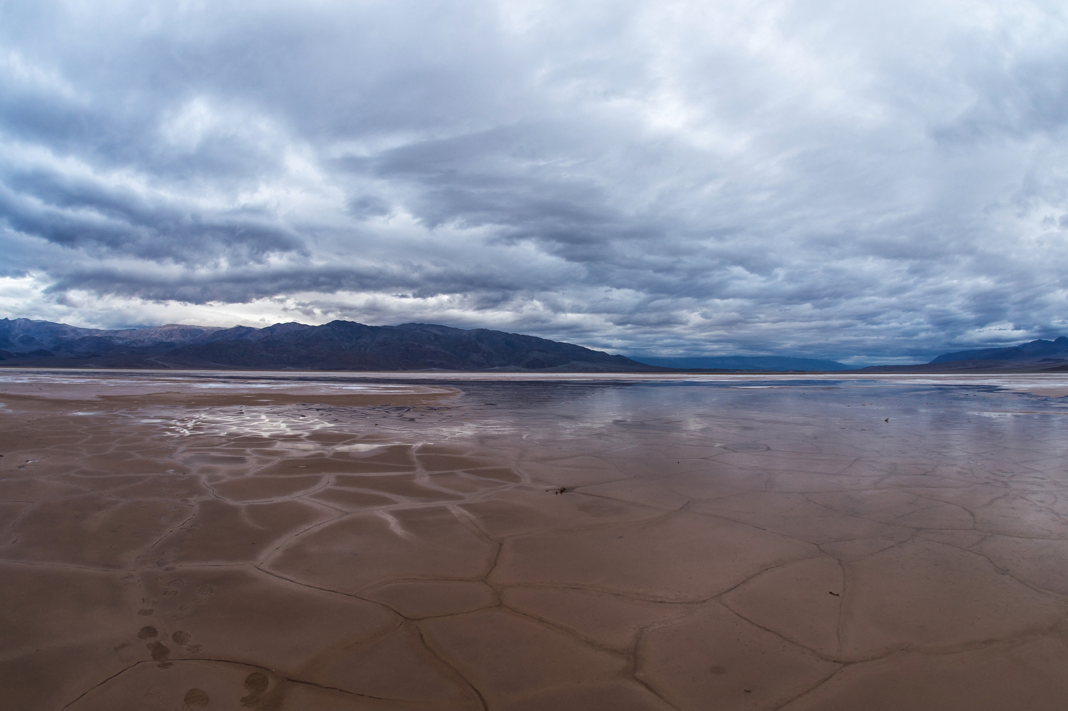 deathvalleynps.jpeg A shallow pool of water over a cracked valley floor underneath a cloudy sky.