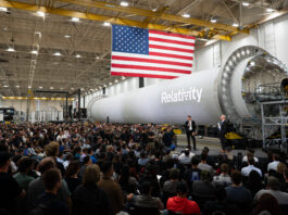 NASA Forms Partnership with Private Sector to Boost Mars Research NASA Administrator Jared Isaacman stands in front of a large, cylindrical, gray spacecraft with a white Relativity logo on it and addresses hundreds of Relativity Space employees. A large American flag hangs from the ceiling.
