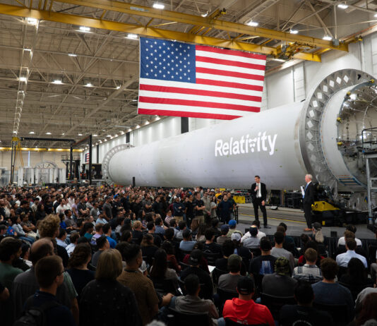 NASA Forms Partnership with Private Sector to Boost Mars Research NASA Administrator Jared Isaacman stands in front of a large, cylindrical, gray spacecraft with a white Relativity logo on it and addresses hundreds of Relativity Space employees. A large American flag hangs from the ceiling.