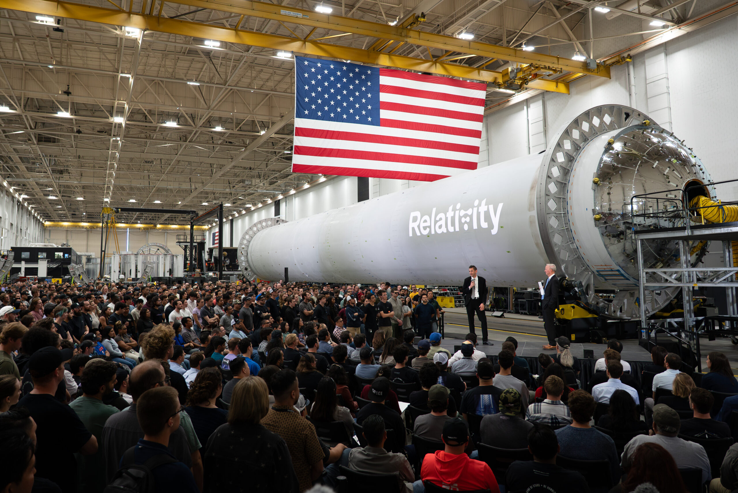 dsc00375 002.jpeg NASA Administrator Jared Isaacman stands in front of a large, cylindrical, gray spacecraft with a white Relativity logo on it and addresses hundreds of Relativity Space employees. A large American flag hangs from the ceiling.