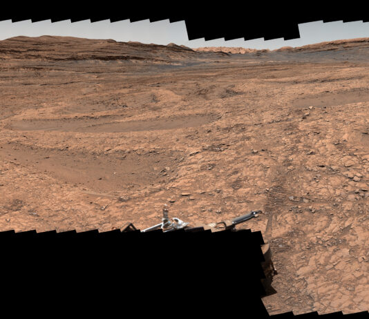 NASA’s Perseverance and Curiosity Showcase Stunning Mars Panoramas A series of shallow, sand-filled pits with low ridges spread across a tawny Martian landscape. Rover tracks stretch toward the horizon at left, and steep ridgetops loom in the background.