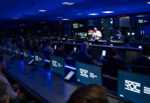 NASA JPL Launches New Center for Lunar and Martian Missions A man, illuminated by white light, talking to a group of people in a room that is otherwise dark and dimly lit with blue light.