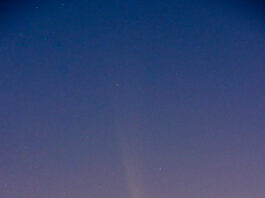 Rare Guest Visits NASA’s Michoud Facility The night sky goes from blue to pink as you look from top to bottom. In the middle is a comet; it looks like a relatively bright yellow dot with a long, diffuse yellow tail. Some stars are visible in the blue portion of the sky.