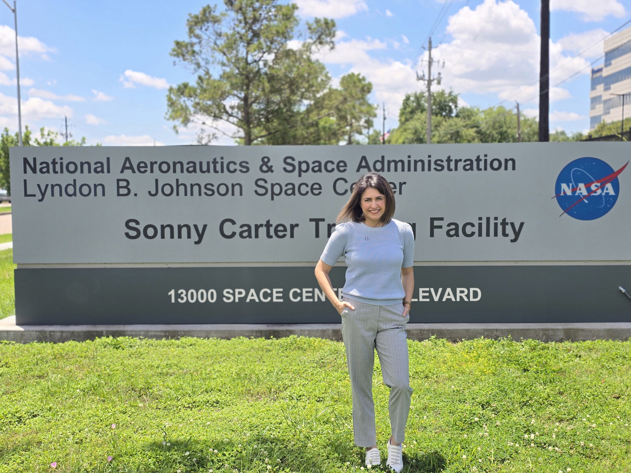 A woman in casual clothes poses in front of a sign for the Johnson Space Center