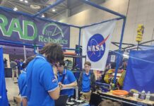 Media Invited to NASA’s Annual FIRST Robotics Competition Students from RAD Robotics Team 7111 – a FIRST Robotics team from Huntsville, Alabama, stand in blue shirts working on their robot with a large NASA meatball logo in the background.