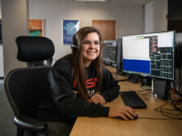 Carissa Arillo: Craft Testing and Writing NASA Manuals Carissa Arillo sits at a table with a monitor and a keyboard, wearing a headset. She smiles at the camera. On the screen is code, but it isn
