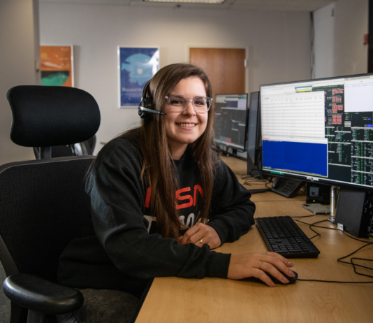 Carissa Arillo: Craft Testing and Writing NASA Manuals Carissa Arillo sits at a table with a monitor and a keyboard, wearing a headset. She smiles at the camera. On the screen is code, but it isn