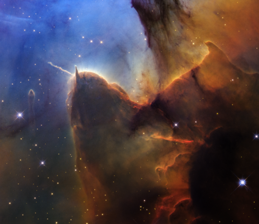 NASA Celebrates the Day of the Trifid Nebula A rich, cosmic landscape is split in two. On the right side, clouds of reddish-black dust billow. On the left, stars sparkle across a dark-blue background.