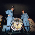 Gemini III: Celebrating 60 Years of Two-Person Spaceflight Two astronauts wearing blue flight suits pose with their space capsule aboard the recovery ship.