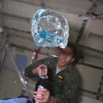 NASA Aircraft Facilitated Groundbreaking ’90s Microgravity Experiments A person in a green flight suit watches as blue fluid floats out of a bottle during a microgravity flight.