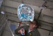 NASA Aircraft Facilitated Groundbreaking ’90s Microgravity Experiments A person in a green flight suit watches as blue fluid floats out of a bottle during a microgravity flight.