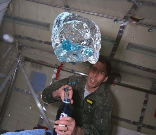 NASA Aircraft Facilitated Groundbreaking ’90s Microgravity Experiments A person in a green flight suit watches as blue fluid floats out of a bottle during a microgravity flight.